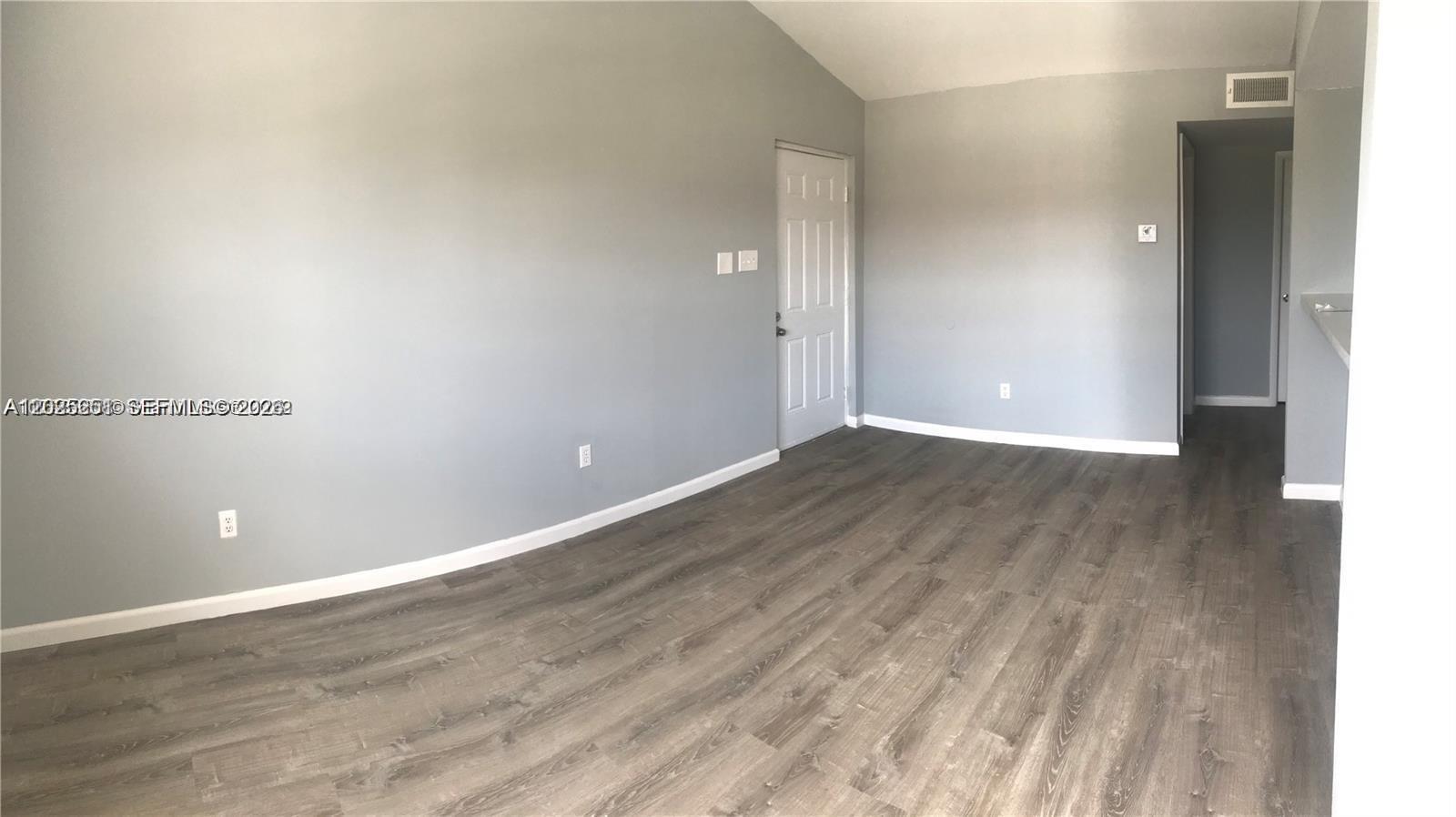 An empty room features gray walls, wood-look flooring, a white door, and a hallway entrance — 15285 SW 107th Ln # 206, Miami FL 33196, MIAMI, FL