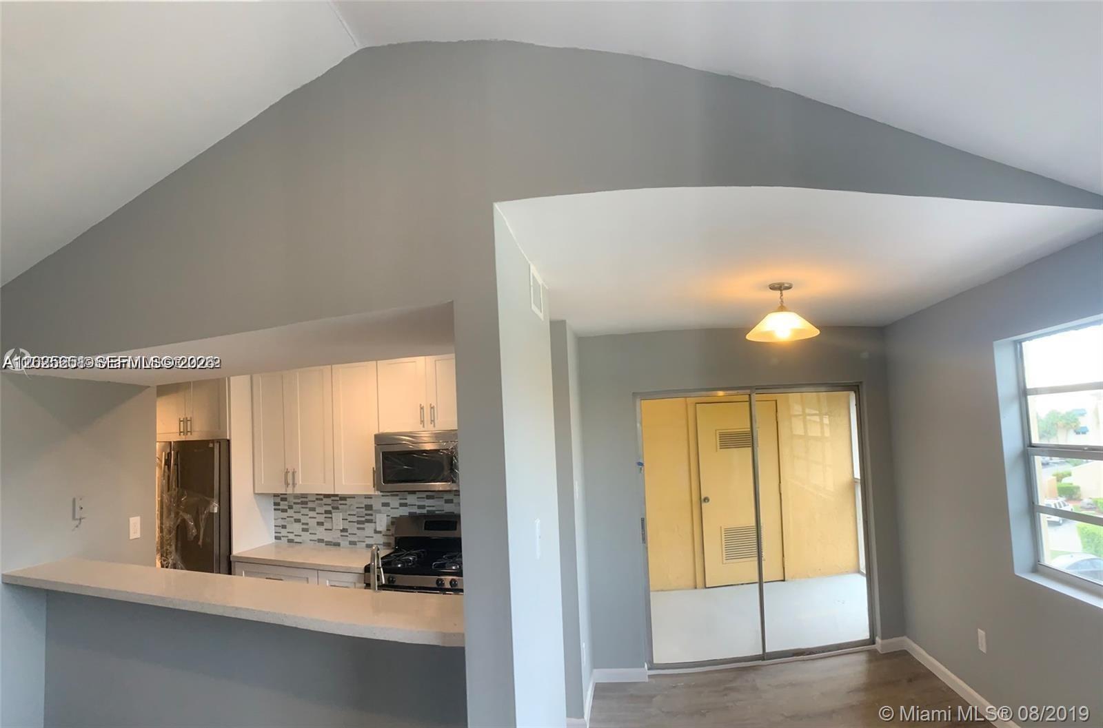 A kitchen with white cabinets and a breakfast bar opens into a dining area — 15285 SW 107th Ln # 206, Miami FL 33196, MIAMI, FL