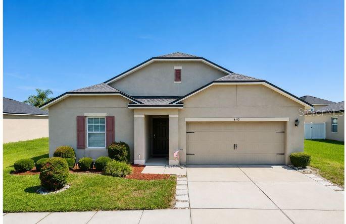 A single-story house with a beige stucco exterior, a two-car garage, and a front lawn — 6103 GREY HERON DRIVE, WINTER HAVEN, FL