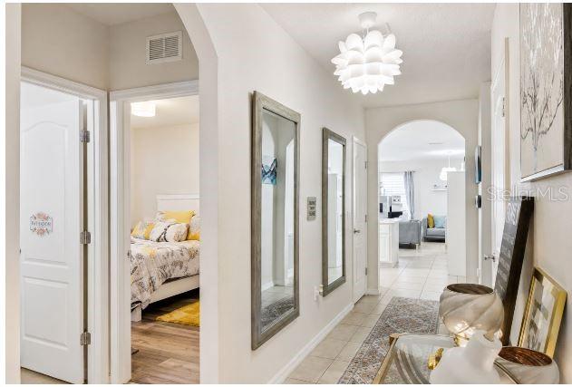 A hallway with tile floors, two wall mirrors, and a view into a bedroom — 6103 GREY HERON DRIVE, WINTER HAVEN, FL