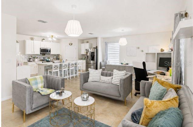 An open-concept living room and kitchen featuring gray sofas, white cabinetry, and tile flooring — 6103 GREY HERON DRIVE, WINTER HAVEN, FL