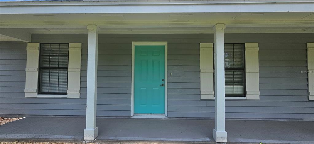A gray house exterior features a bright teal front door and white shutters on windows — 2625 SPRING VALLEY CIRCLE, DELAND, FL