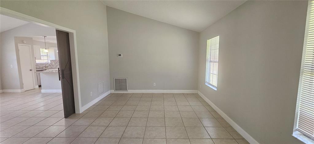 A room with light-colored tile flooring, a vaulted ceiling, and a sliding barn door — 2625 SPRING VALLEY CIRCLE, DELAND, FL