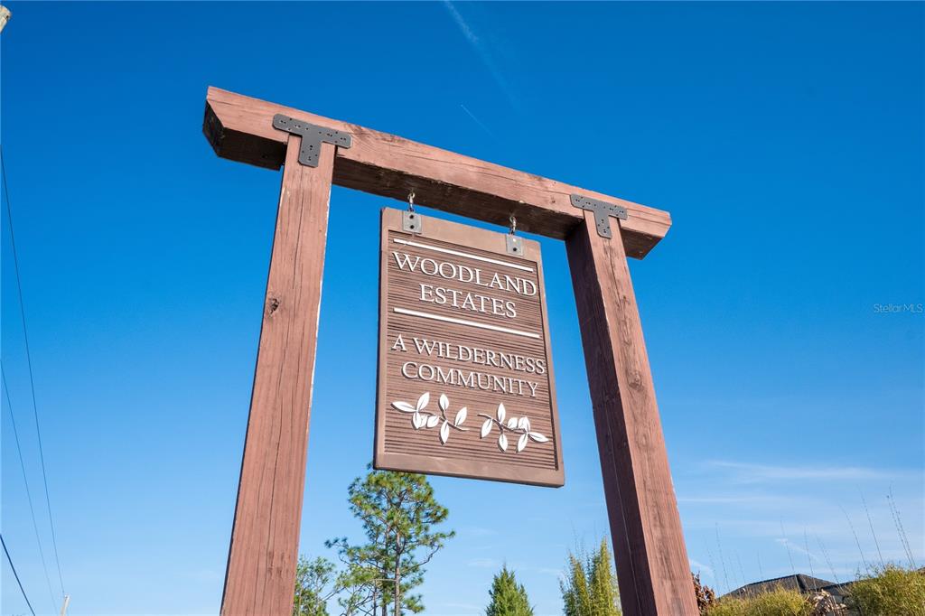 A wooden sign for Woodland Estates hangs from a tall, rustic post against a blue sky — 2468 FAWN RUN, OVIEDO, FL
