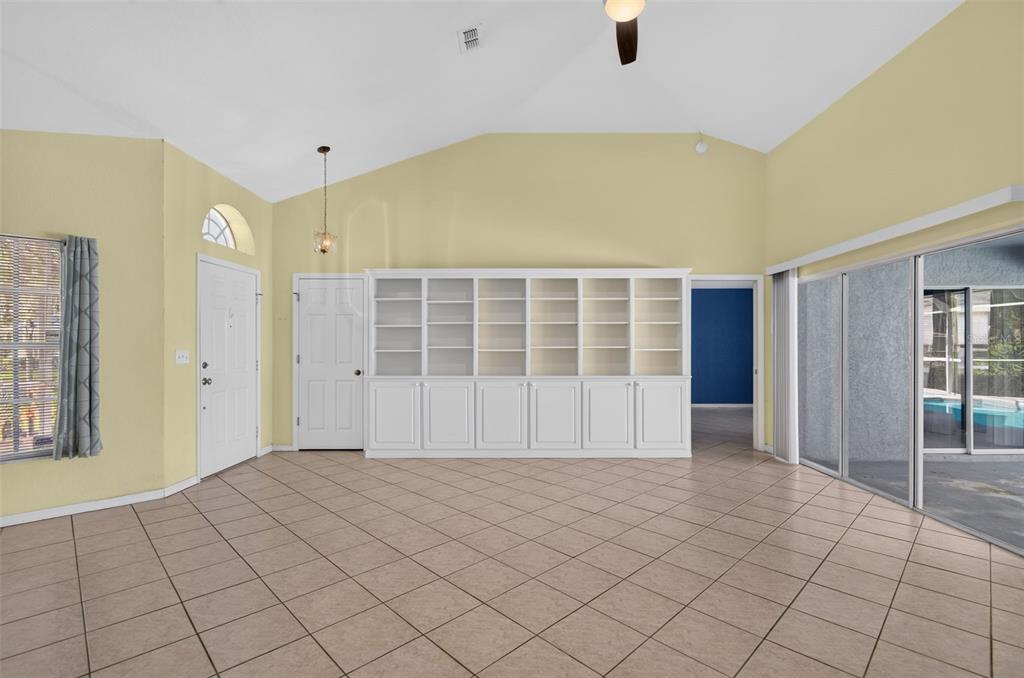 A living room with yellow walls, tile flooring, a built-in bookshelf, and sliding glass doors — 2791 GOLF LAKE DRIVE UNIT 55, PLANT CITY, FL