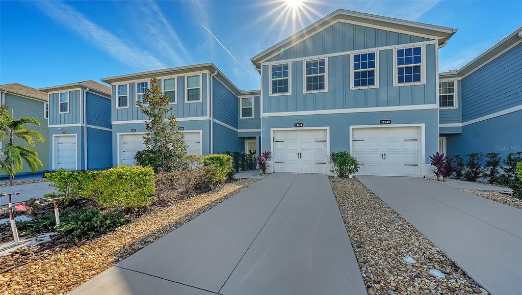 A two-story blue townhouse exterior features two garage doors and a concrete driveway — 14244 CRIMSON AVENUE, BRADENTON, FL