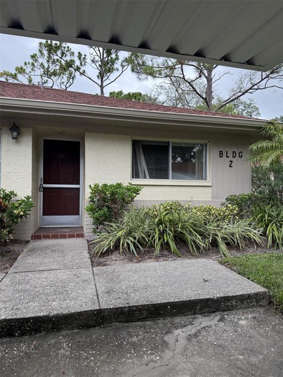 The exterior of a single-story residential building features a maroon door, a window, and landscaping — 2460 NORTHSIDE DRIVE UNIT 206, CLEARWATER, FL
