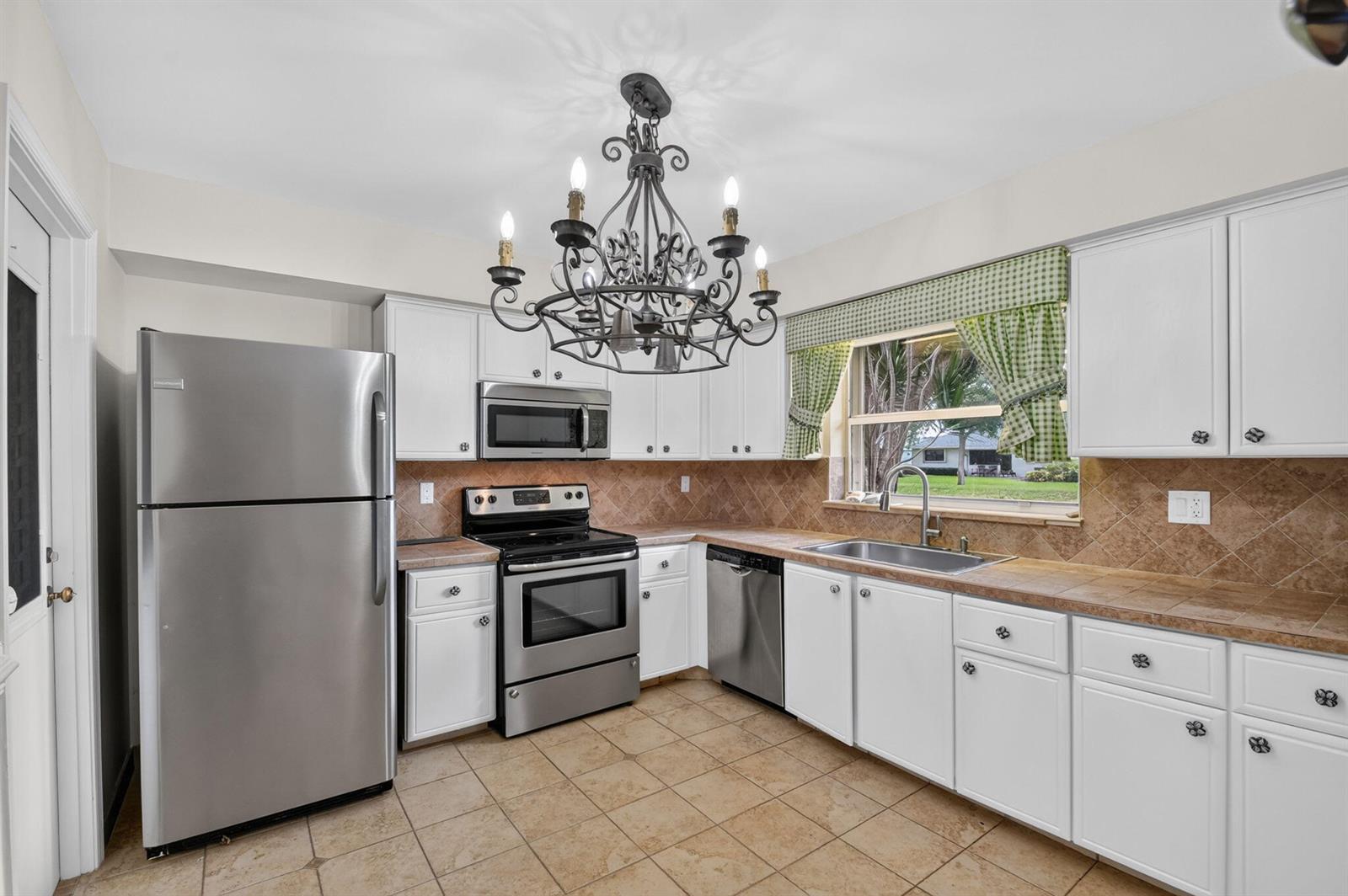 A kitchen with white cabinets, stainless steel appliances, tile countertops, and a decorative chandelier — 9930 Frangipani Tree Way # B, Boynton Beach FL 33436, BOYNTON BEACH, FL