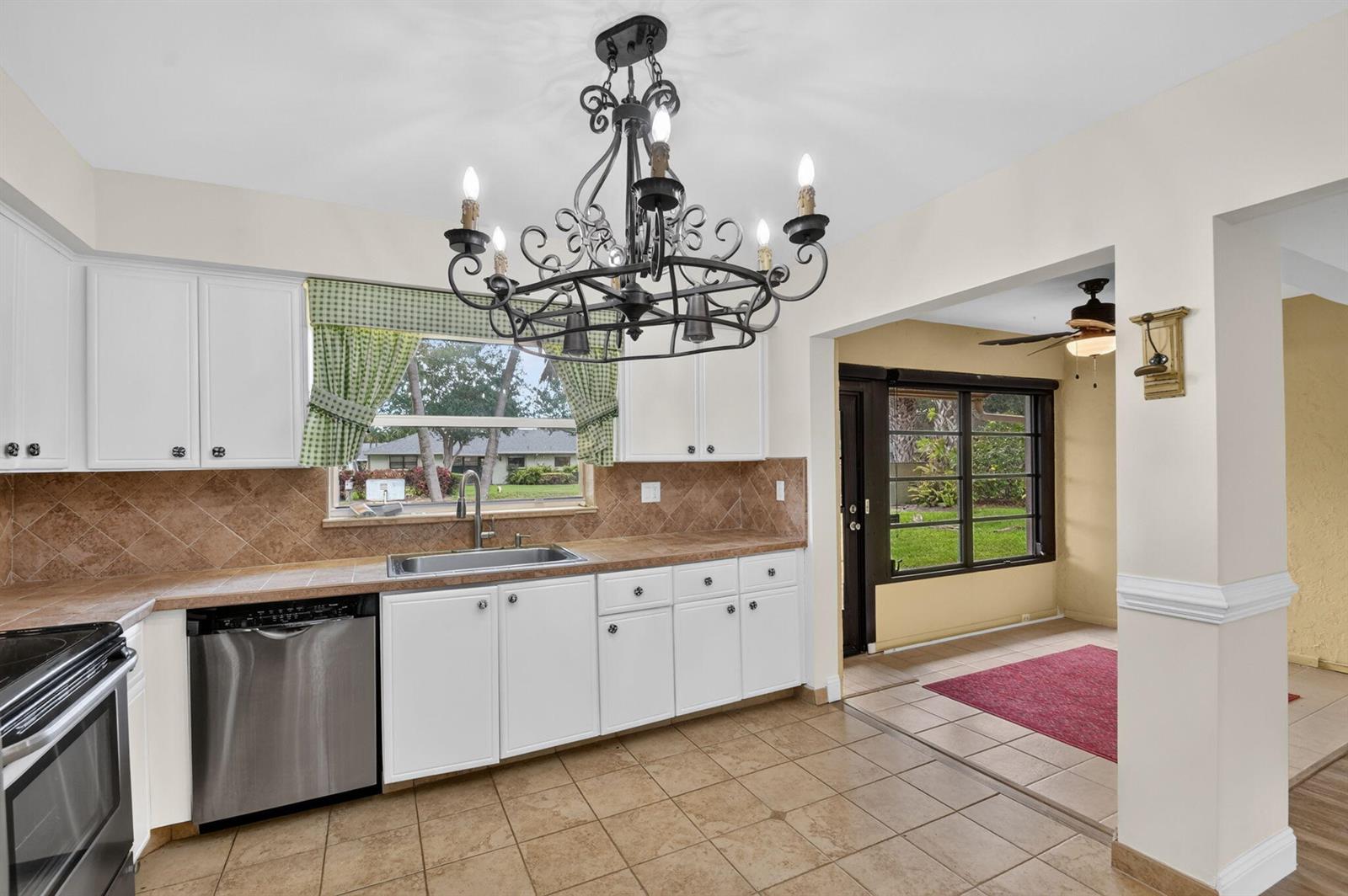 A kitchen with white cabinets, tile countertops, a stainless dishwasher, and a large chandelier — 9930 Frangipani Tree Way # B, Boynton Beach FL 33436, BOYNTON BEACH, FL