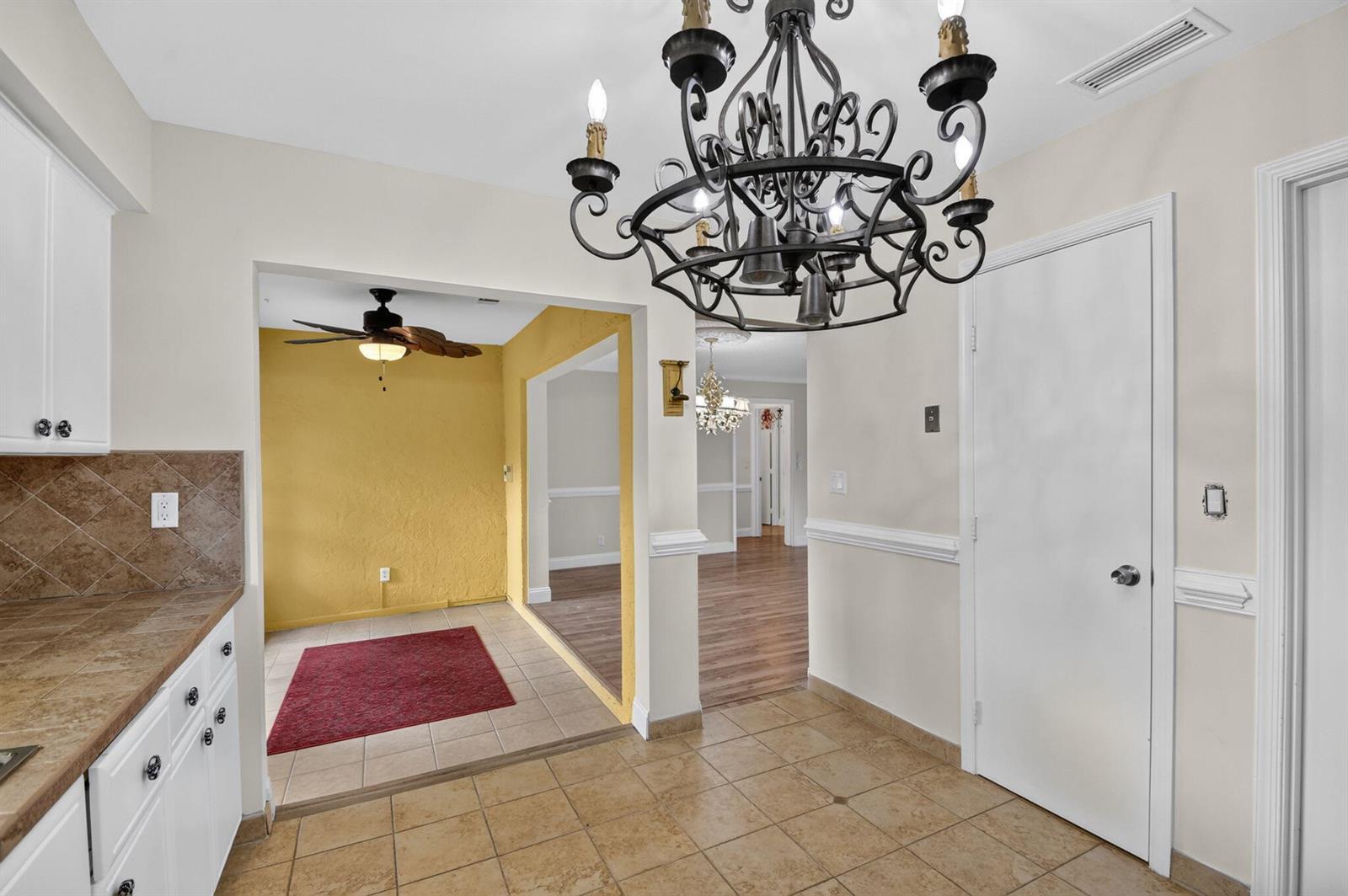 A kitchen with tile flooring and a chandelier leads into a yellow-walled dining area — 9930 Frangipani Tree Way # B, Boynton Beach FL 33436, BOYNTON BEACH, FL