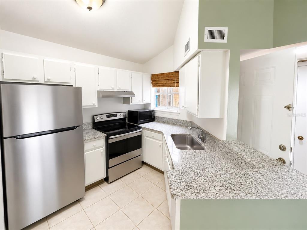 A kitchen features white cabinets, granite countertops, stainless steel appliances, and light-colored tile flooring — 1908 LAKE ATRIUMS CIRCLE UNIT 9, ORLANDO, FL