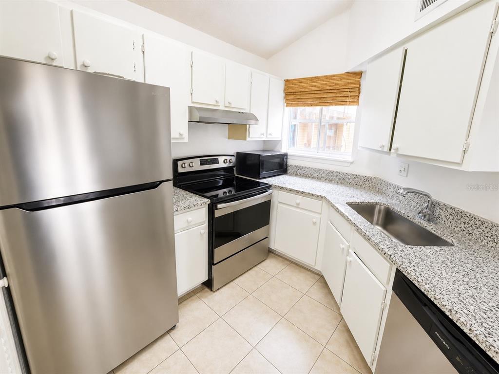 A kitchen features stainless steel appliances, white cabinets, and speckled granite countertops — 1908 LAKE ATRIUMS CIRCLE UNIT 9, ORLANDO, FL