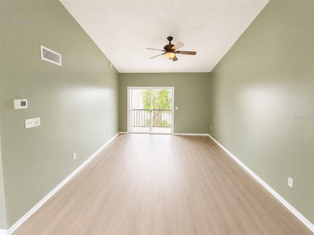 An empty room with sage green walls, light wood-look flooring, and a sliding glass door — 1908 LAKE ATRIUMS CIRCLE UNIT 9, ORLANDO, FL