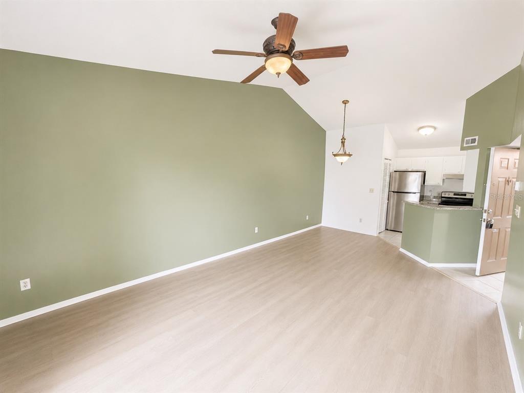 A living room with a vaulted ceiling, sage green accent wall, and light wood flooring — 1908 LAKE ATRIUMS CIRCLE UNIT 9, ORLANDO, FL