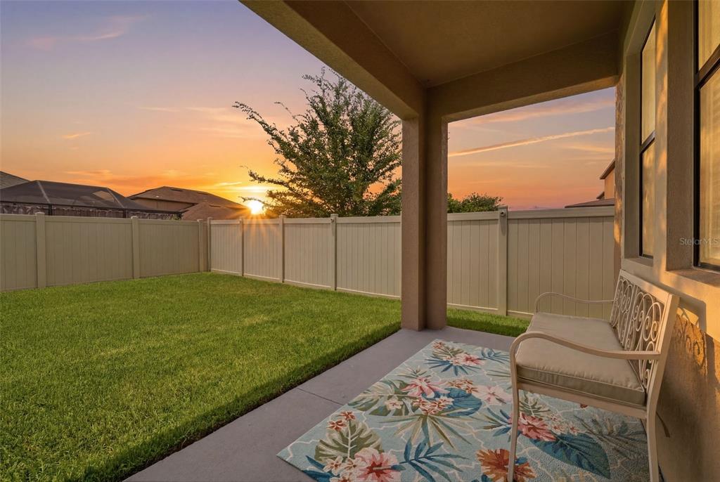 A covered patio with a floral rug and bench overlooks a fenced backyard at sunset — 9927 IVORY DRIVE, RUSKIN, FL