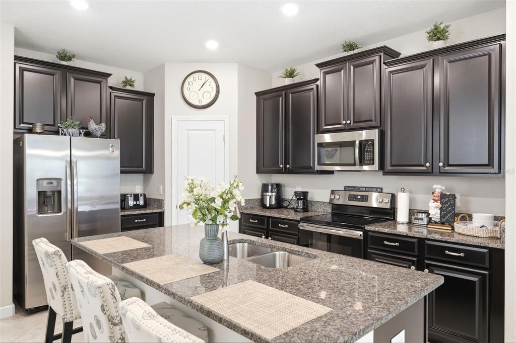 A kitchen features dark wood cabinets, granite countertops, stainless steel appliances, and a central island — 9927 IVORY DRIVE, RUSKIN, FL