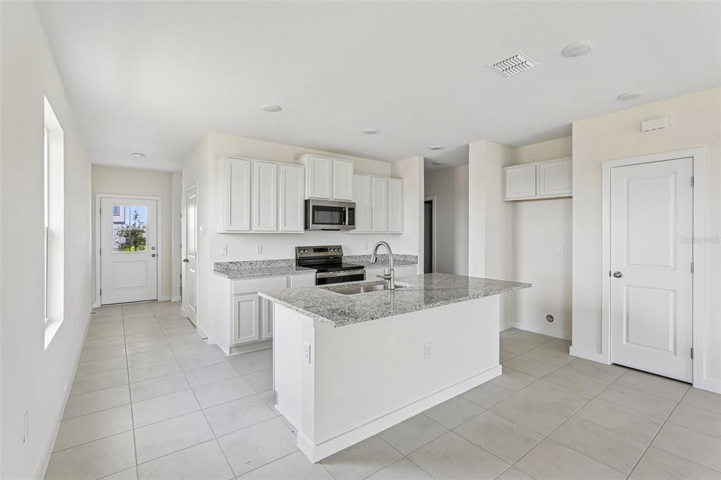 A modern kitchen features white cabinets, granite countertops, a central island, and light tile flooring — 1940 DIAMOND HEAD CIRCLE, HAINES CITY, FL