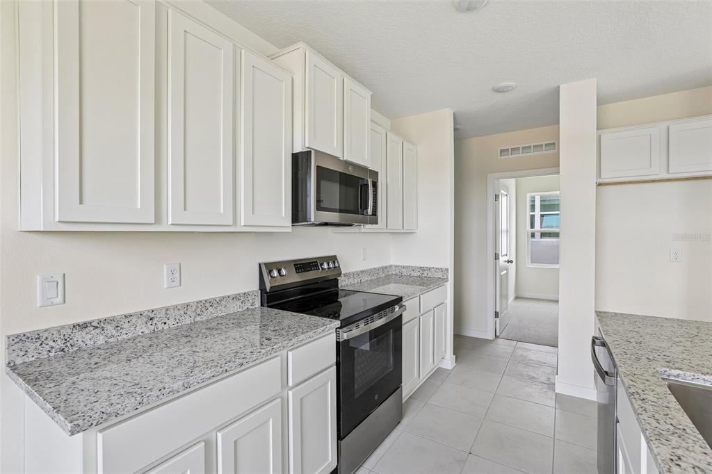A kitchen features white cabinets, granite countertops, stainless steel appliances, and light tile flooring — 1940 DIAMOND HEAD CIRCLE, HAINES CITY, FL