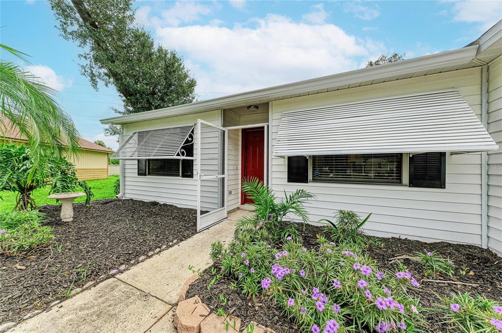The exterior of a single-story house features white horizontal siding, metal window awnings, and landscaping — 5506 82ND AVENUE DRIVE E, PALMETTO, FL