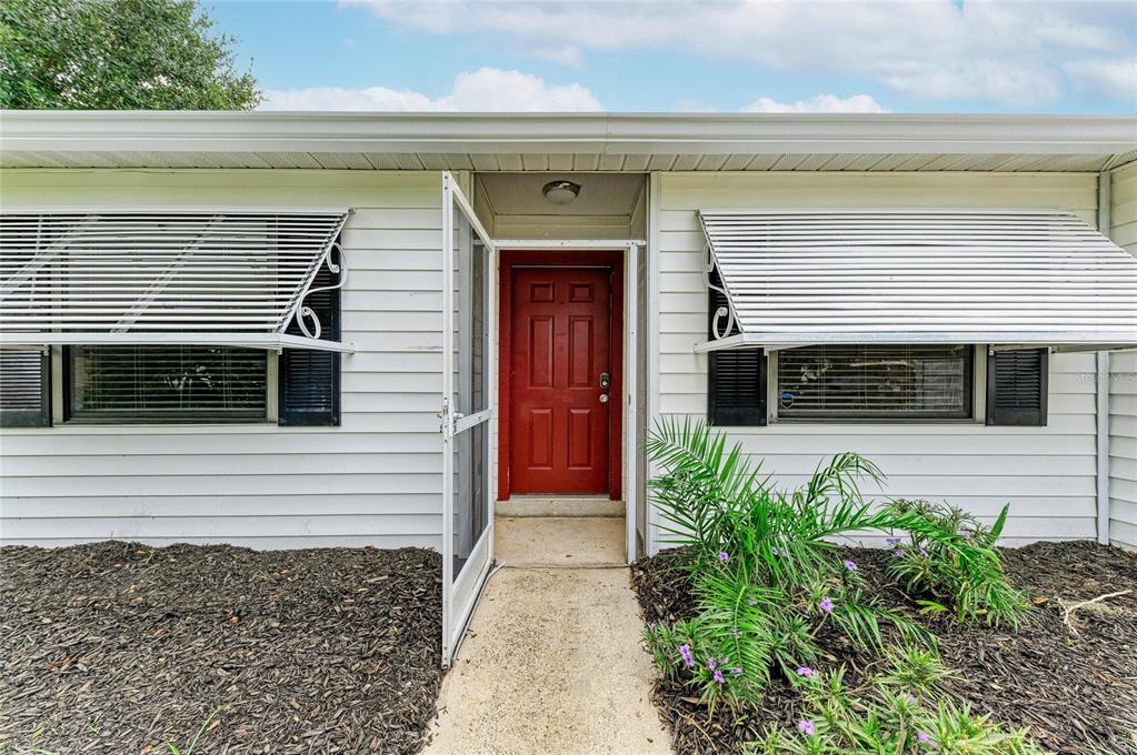 A white house exterior features a red front door, metal awnings, and a concrete walkway — 5506 82ND AVENUE DRIVE E, PALMETTO, FL