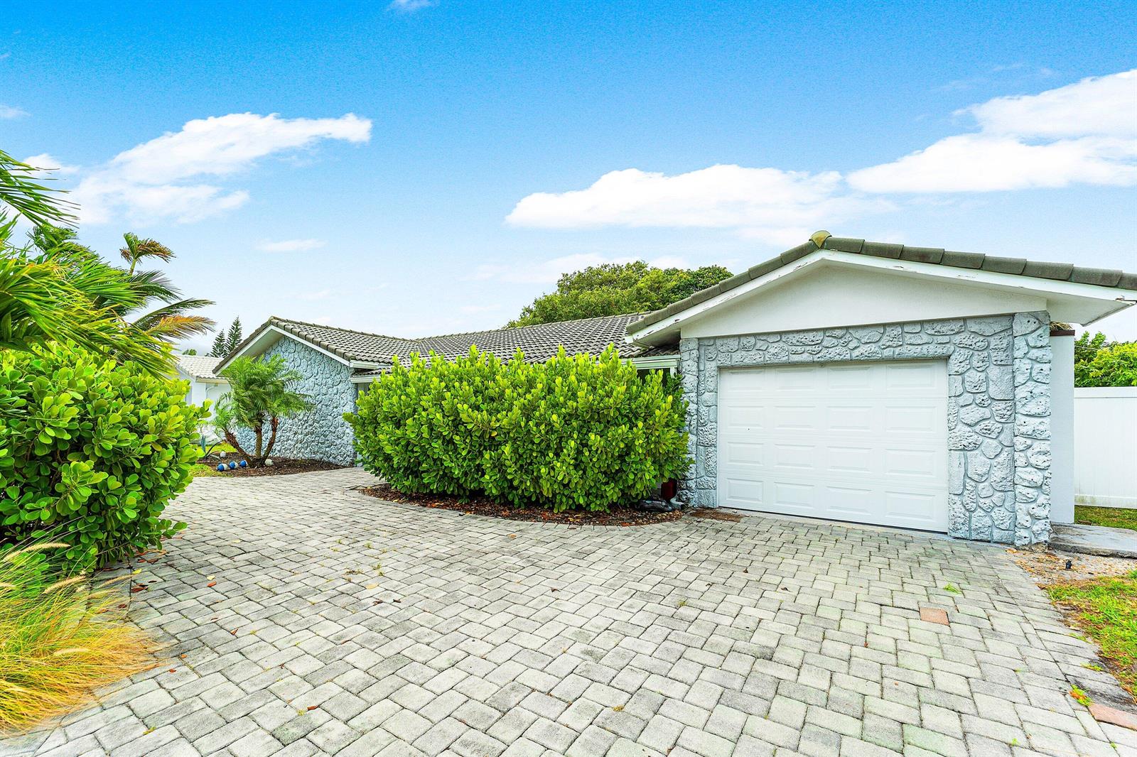 A single-story house with a stone facade, a white garage door, and a paved driveway — 581 NW 13th Drive, Boca Raton FL 33486, BOCA RATON, FL