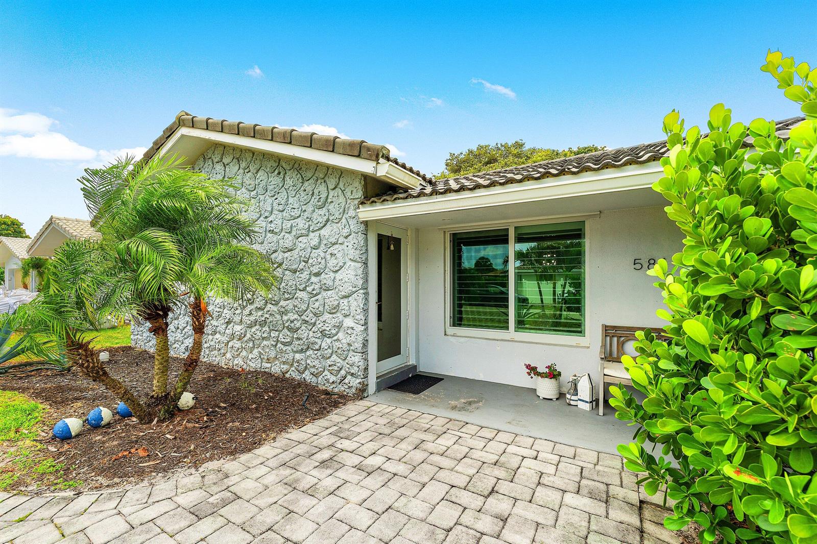 A single-story home exterior features a stone facade, a paved walkway, and a palm tree — 581 NW 13th Drive, Boca Raton FL 33486, BOCA RATON, FL