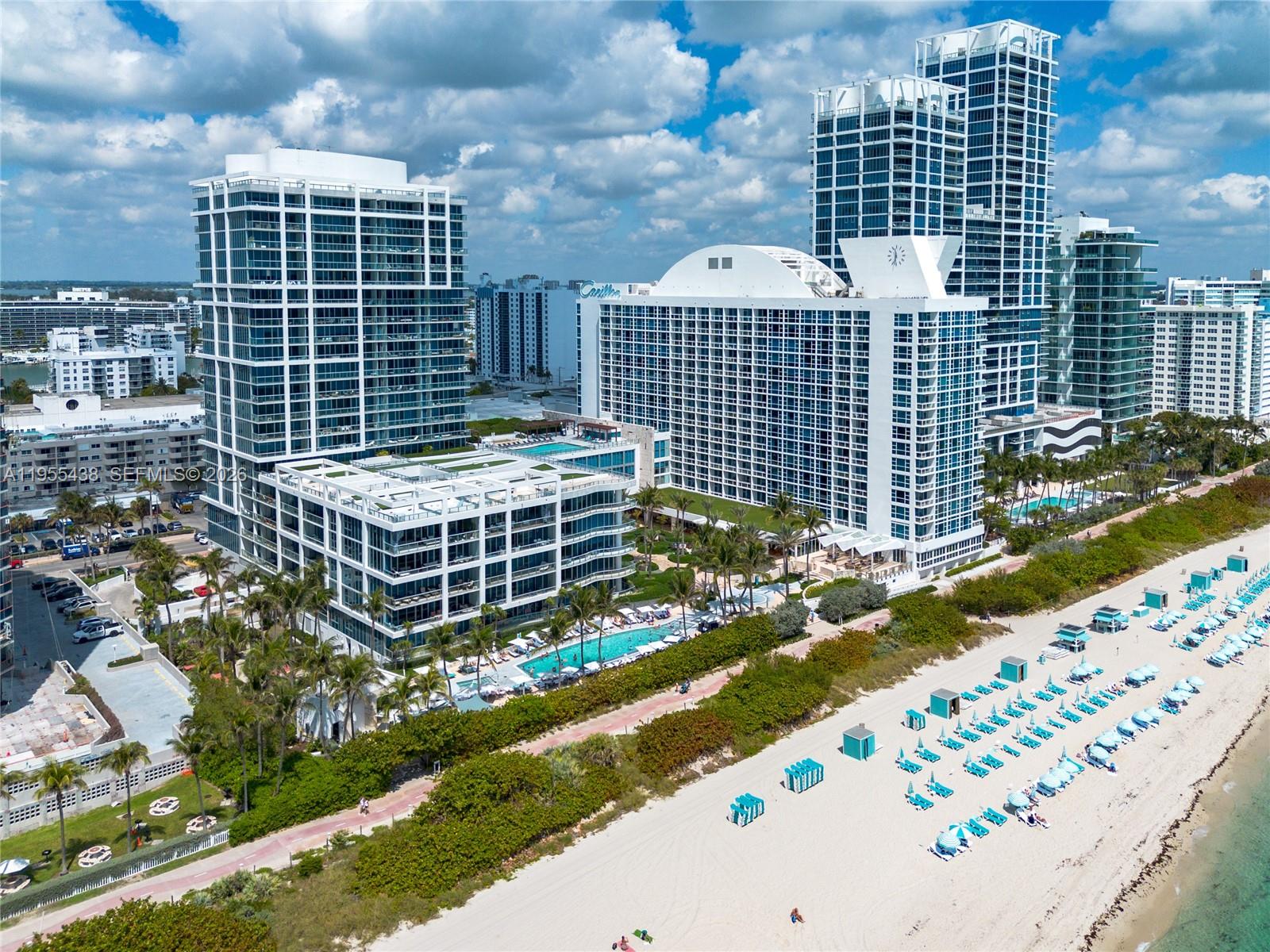 An aerial view shows several high-rise buildings situated along a sandy beach with palm trees — 6799 Collins Ave # 401, Miami Beach FL 33141, MIAMI BEACH, FL