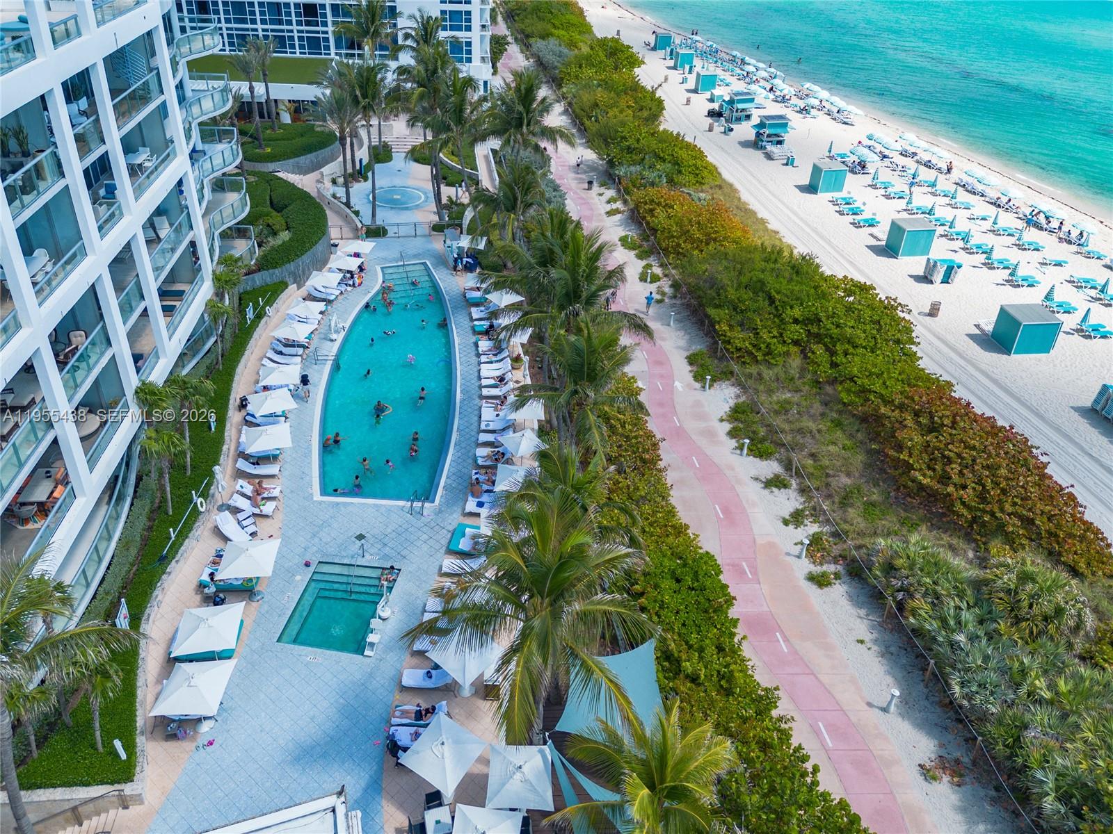 An aerial view shows a resort swimming pool, lounge chairs, and a beach with umbrellas — 6799 Collins Ave # 401, Miami Beach FL 33141, MIAMI BEACH, FL