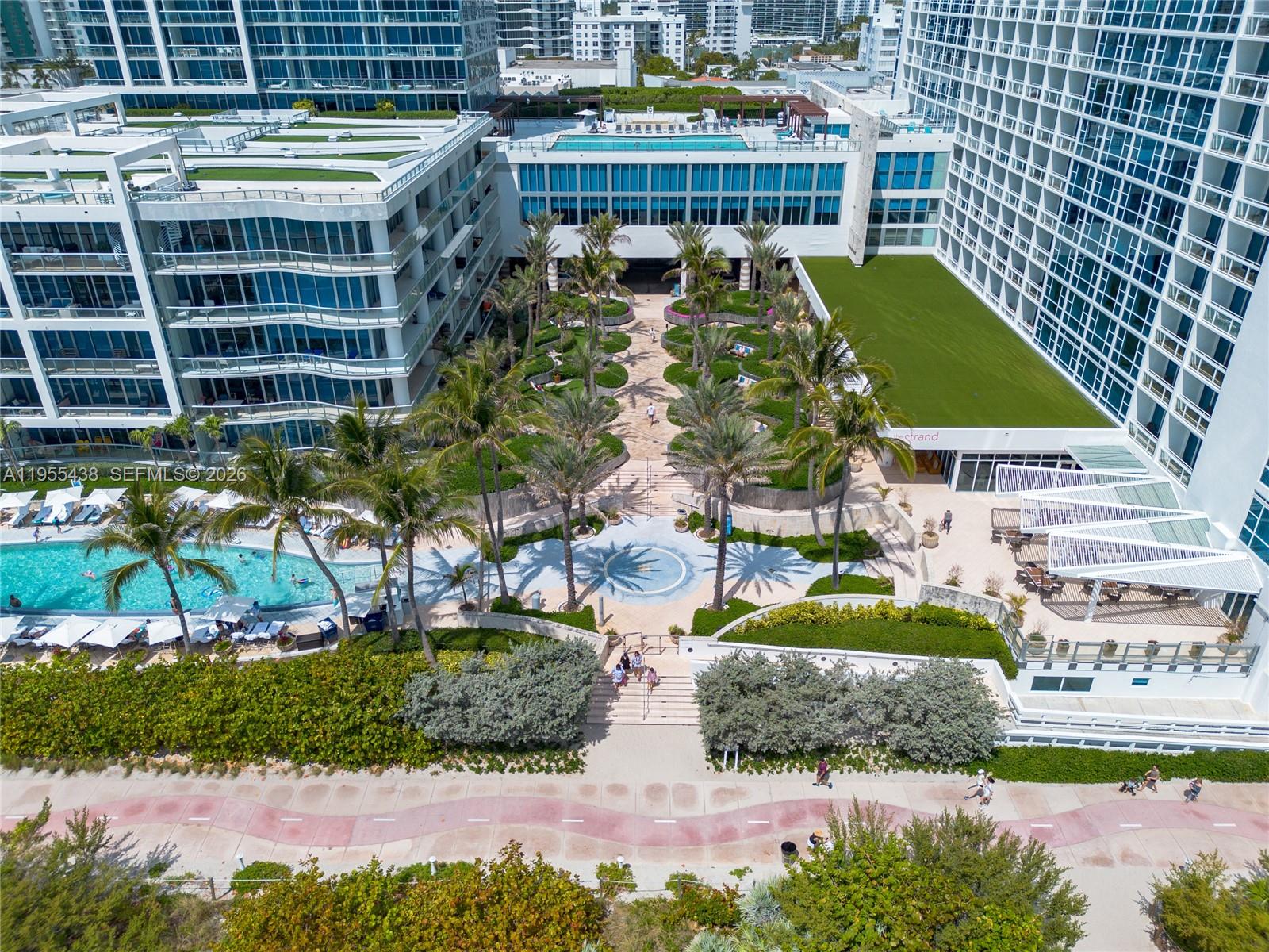 An aerial view shows a resort complex with a swimming pool, palm trees, and walkways — 6799 Collins Ave # 401, Miami Beach FL 33141, MIAMI BEACH, FL