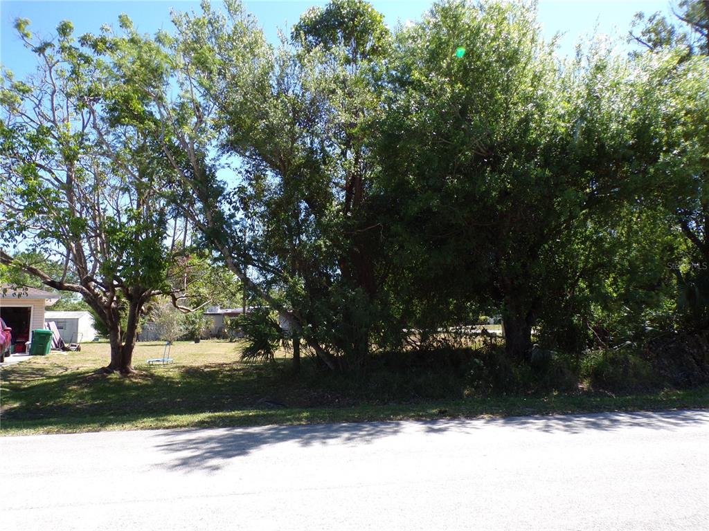 A vacant, tree-covered residential lot sits next to a house with a garage — 4704 FAIRWAY DRIVE N, PUNTA GORDA, FL