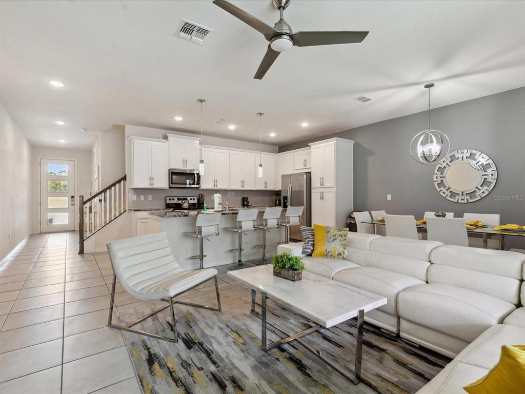 An open-concept kitchen and living area features white cabinetry, a breakfast bar, and white furniture — 1632 TROPICAL PALMS CIRCLE, KISSIMMEE, FL