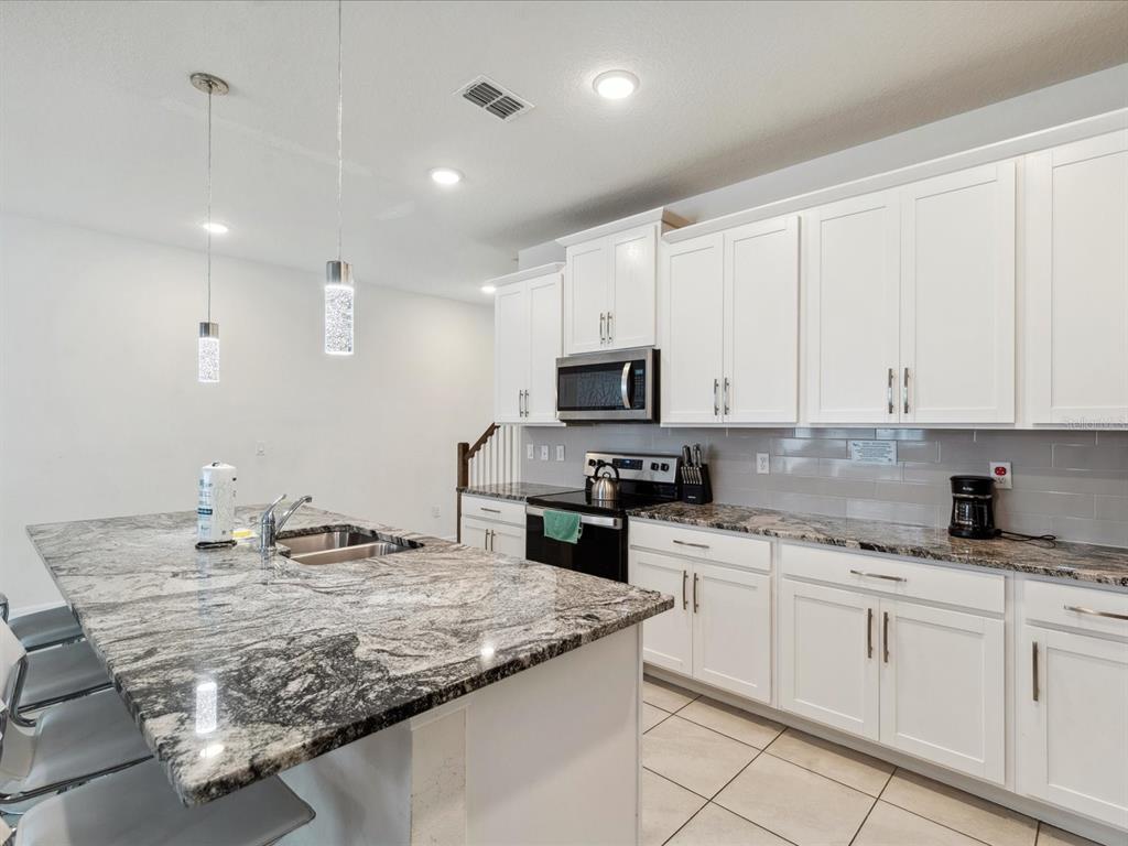 A kitchen features white cabinets, granite countertops, a large island, and stainless steel appliances — 1632 TROPICAL PALMS CIRCLE, KISSIMMEE, FL