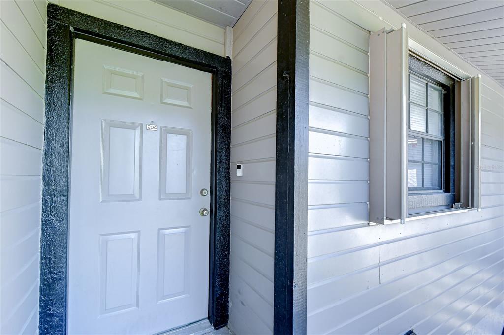 A white front door with a number 204 sign sits beside a window with shutters — 4008 ASHFORD GREEN PLACE UNIT F204, TAMPA, FL