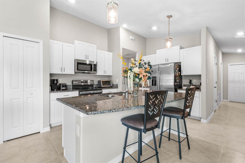 A kitchen features white cabinets, granite countertops, a center island with bar stools, and stainless appliances — 15477 MILLER CREEK DRIVE, SUN CITY CENTER, FL