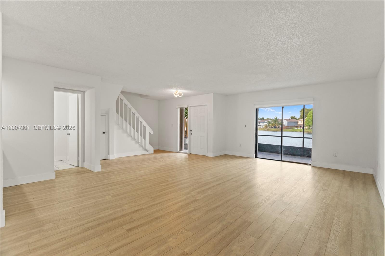 An empty living room features light wood-look flooring, white walls, a staircase, and sliding doors — 6745 NW 169th St # G, Hialeah FL 33015, HIALEAH, FL