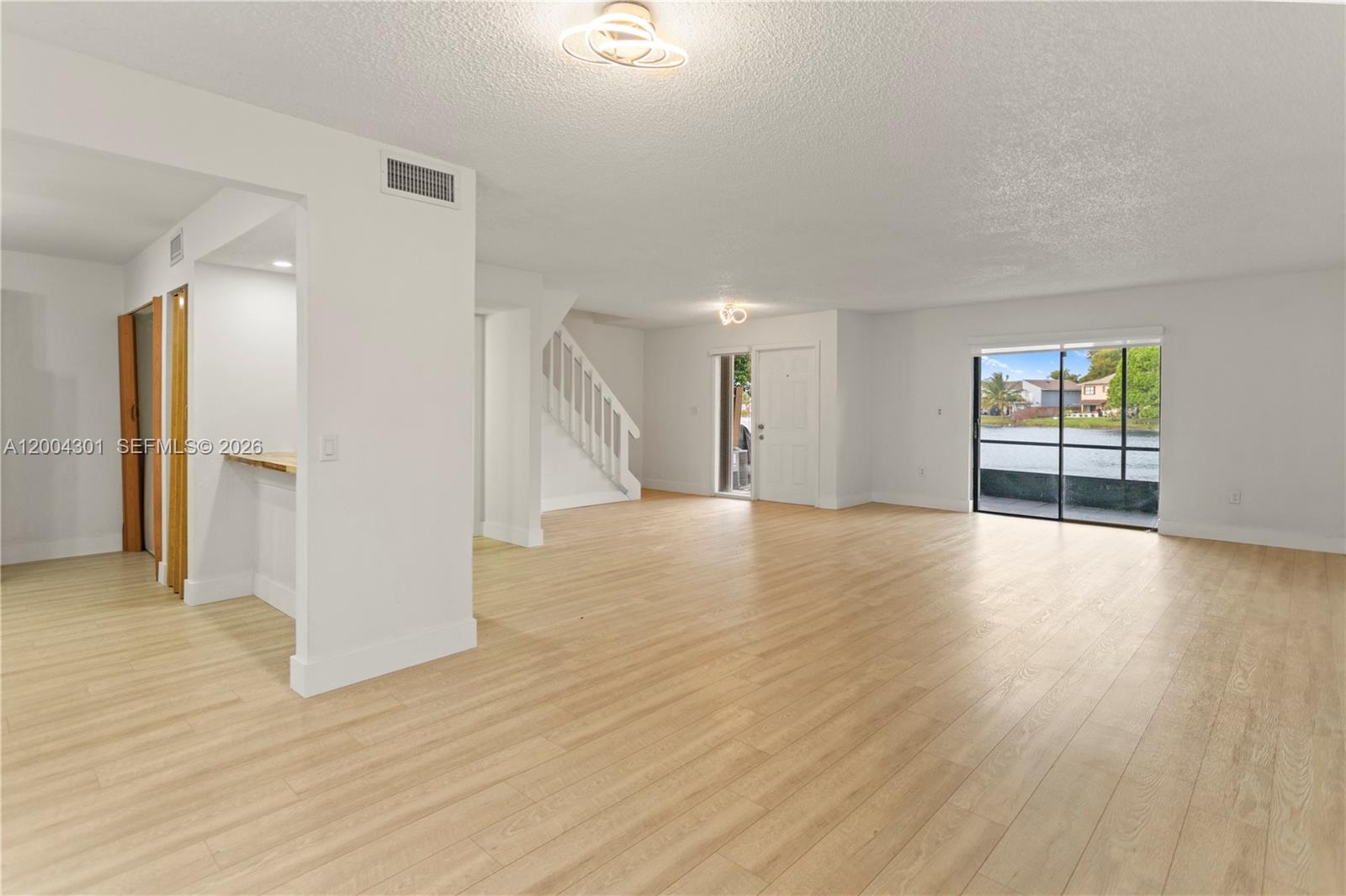 An open-concept living area features light wood flooring, a staircase, and a sliding glass door — 6745 NW 169th St # G, Hialeah FL 33015, HIALEAH, FL