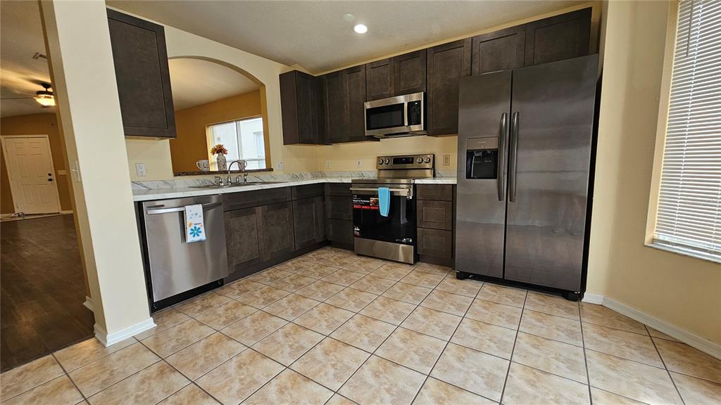 A kitchen features dark wood cabinets, stainless steel appliances, and light-colored tile flooring — 12629 EVINGTON POINT DRIVE, RIVERVIEW, FL