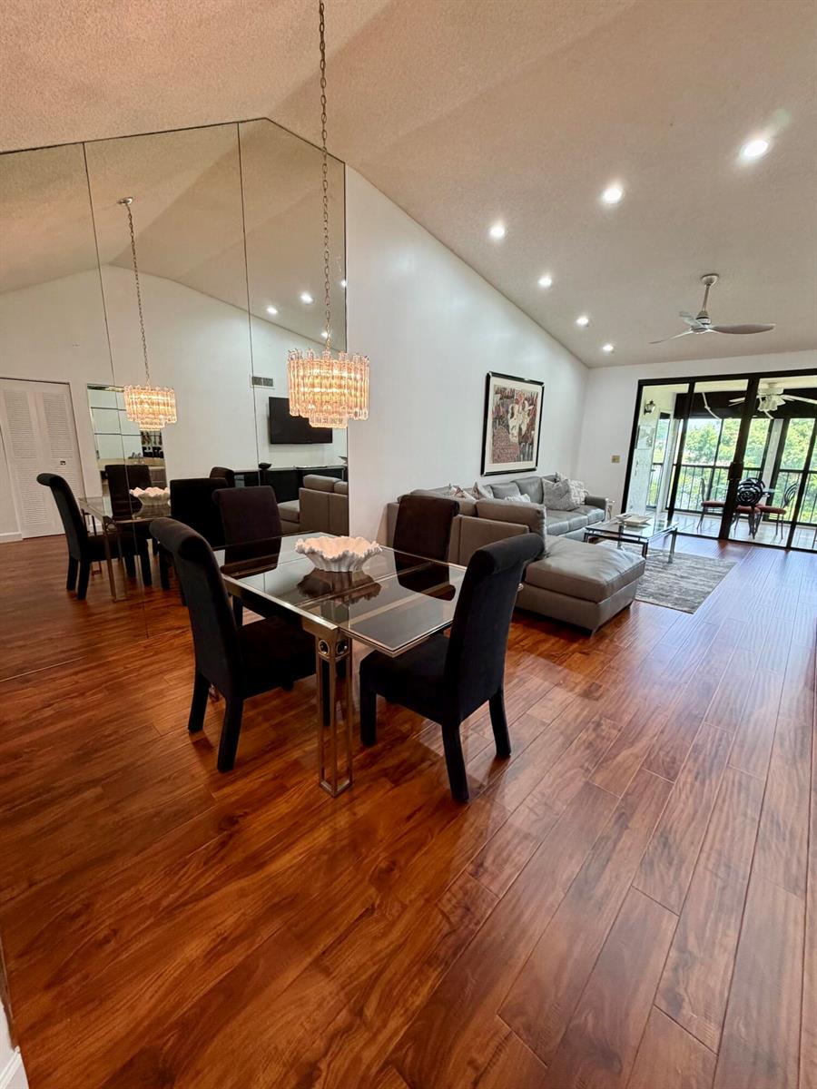 An open-concept living and dining area features hardwood floors, vaulted ceilings, and a mirrored wall — 15758 Loch Maree Lane # 4005, Delray Beach FL 33446, DELRAY BEACH, FL
