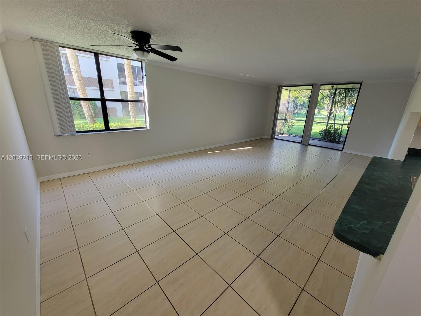 An empty living room features light-colored tile flooring, a ceiling fan, and large windows — PLANTATION, FL