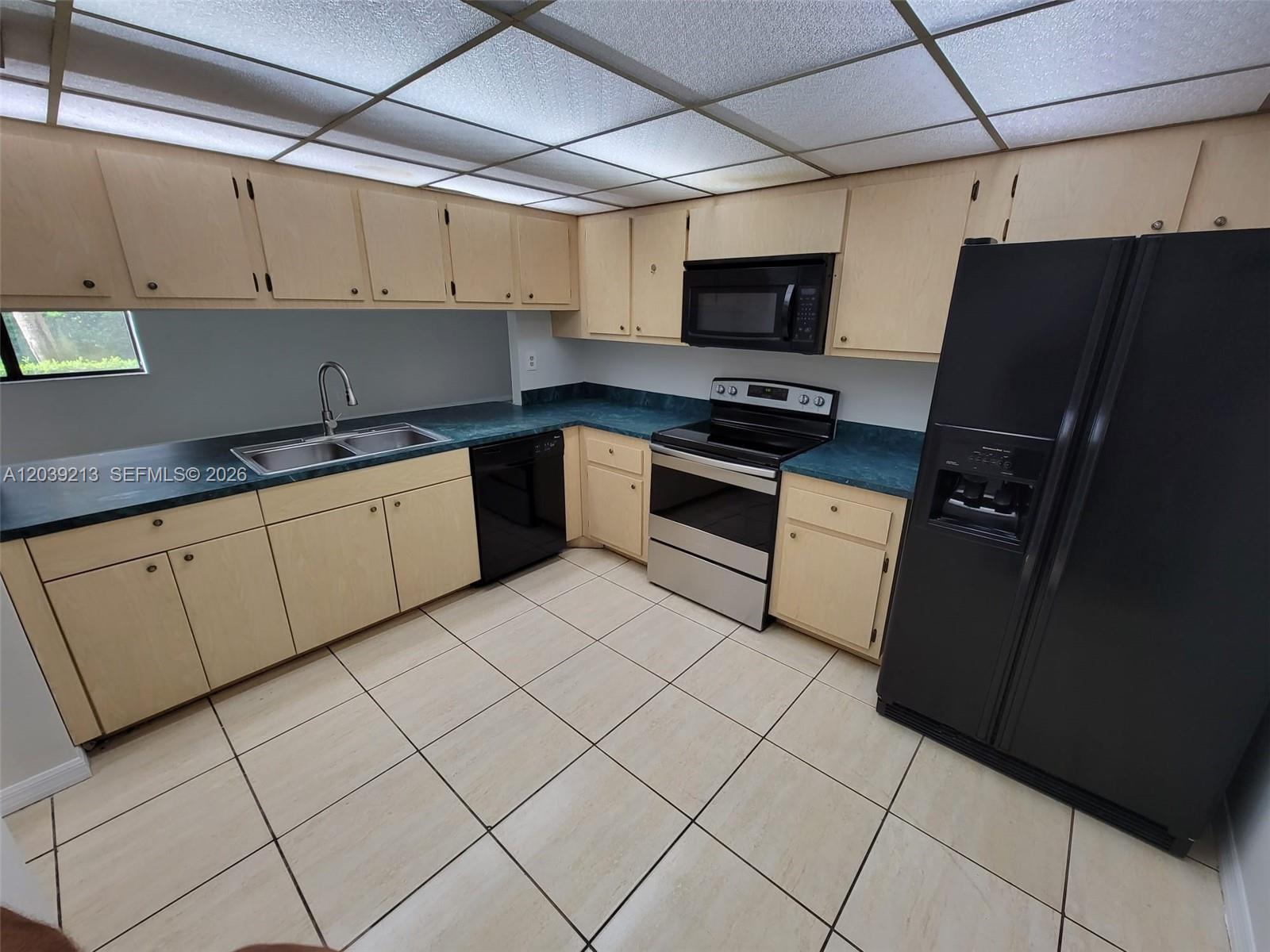 A kitchen features light wood cabinets, dark countertops, black appliances, and a tiled floor — PLANTATION, FL
