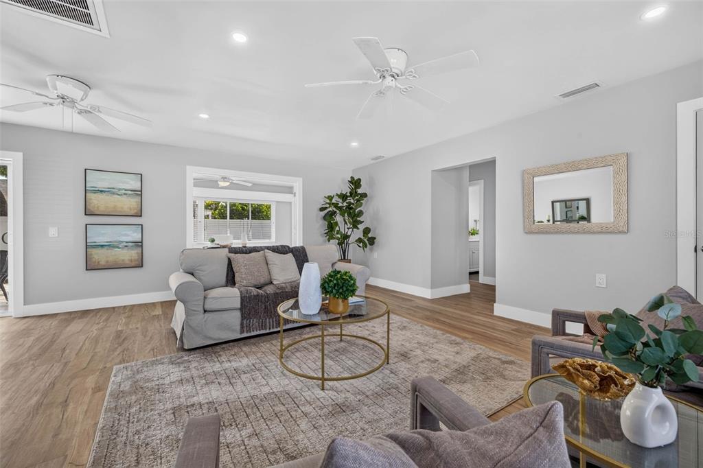 A living room features light gray walls, wood-look flooring, a sofa, and two ceiling fans — 8651 GULF BOULEVARD, ST PETE BEACH, FL