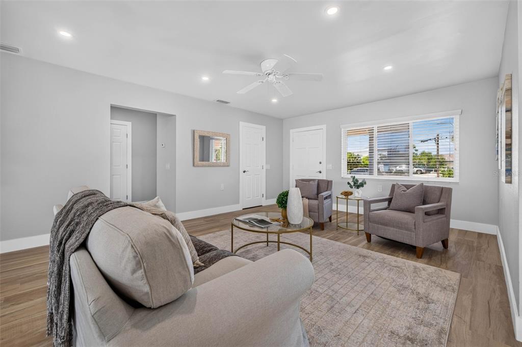 A living room features light gray walls, wood-look flooring, a ceiling fan, and neutral furniture — 8651 GULF BOULEVARD, ST PETE BEACH, FL