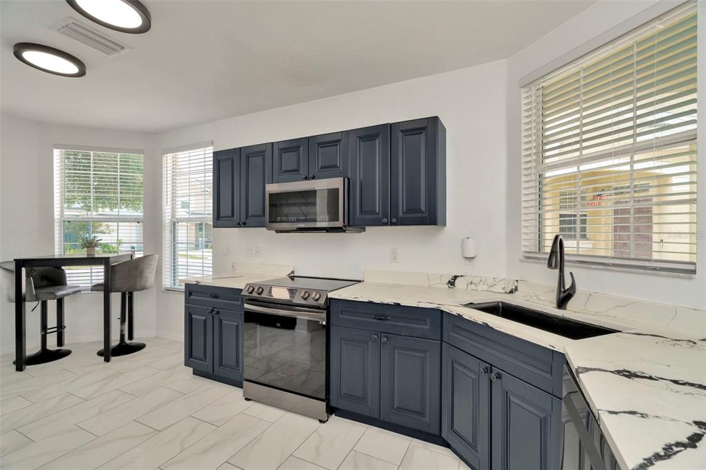 A kitchen features dark blue cabinets, white marble-look countertops, and stainless steel appliances — 6233 OLIVEDALE DRIVE, RIVERVIEW, FL