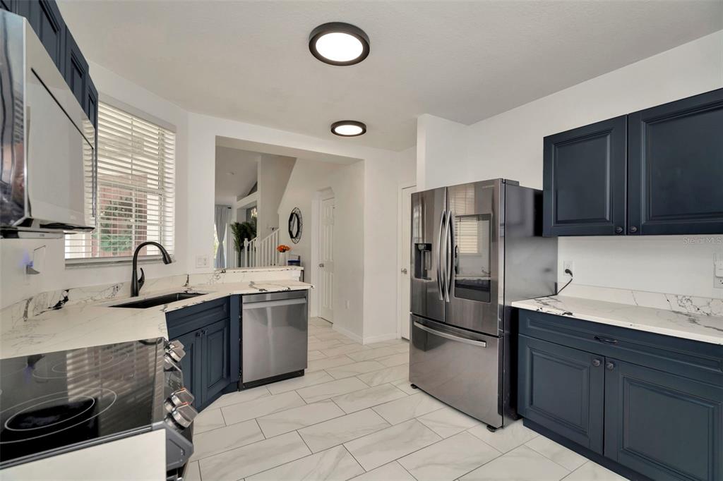A kitchen features dark blue cabinets, white marble-look countertops, stainless steel appliances, and tiled flooring — 6233 OLIVEDALE DRIVE, RIVERVIEW, FL