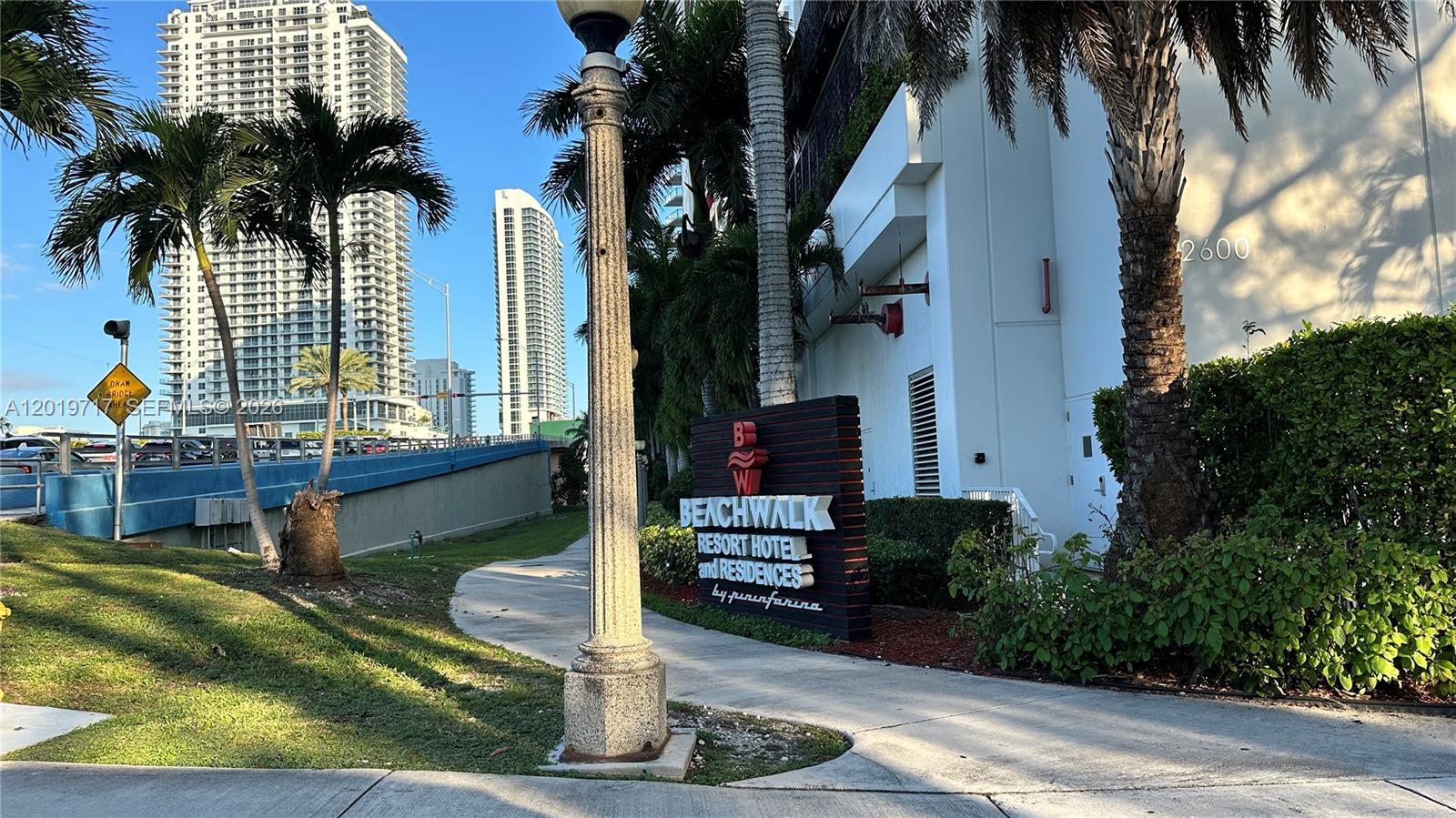 A sign for Beachwalk Resort Hotel and Residences stands on a sidewalk near palm trees — 2602 E Hallandale Beach Blvd # R703, Hallandale Beach FL 33009, HALLANDALE BEACH, FL