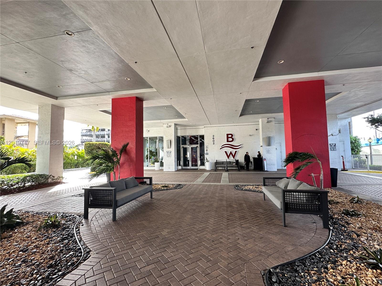 A covered building entrance features two red pillars, outdoor seating, and a paved driveway — 2602 E Hallandale Beach Blvd # R703, Hallandale Beach FL 33009, HALLANDALE BEACH, FL