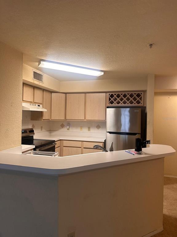 A kitchen features light wood cabinets, white countertops, stainless steel appliances, and a breakfast bar — 820 CAMARGO WAY UNIT 207, ALTAMONTE SPRINGS, FL