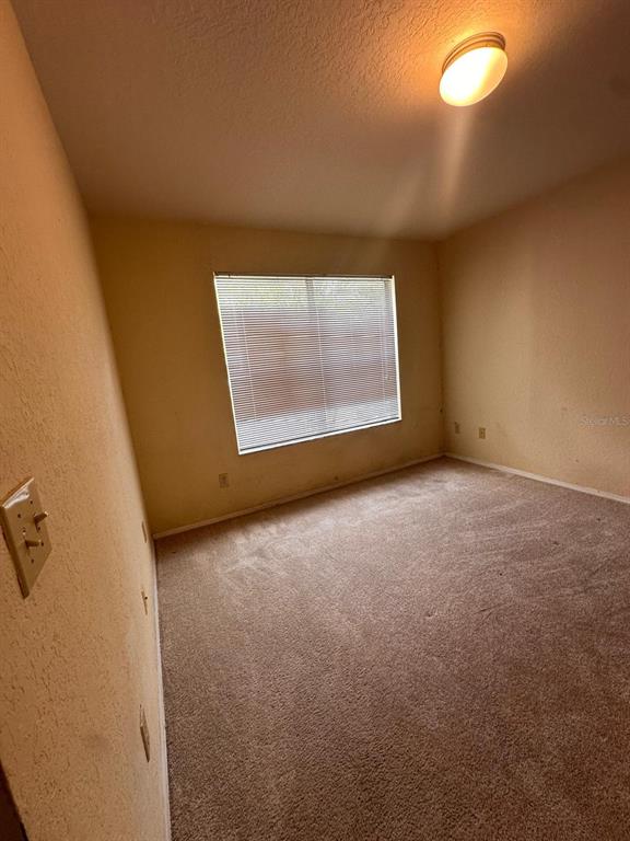 An empty bedroom features beige walls, tan carpeting, a single window with blinds, and a light — 820 CAMARGO WAY UNIT 207, ALTAMONTE SPRINGS, FL