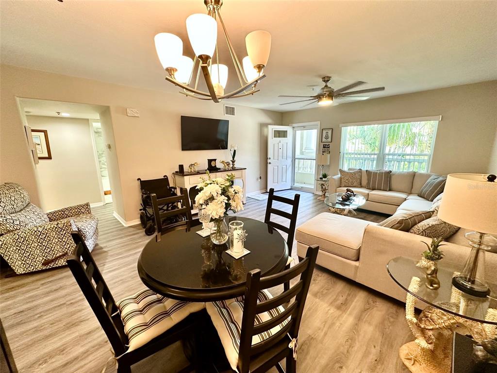 A living and dining area features light wood-look flooring, a chandelier, and a sectional sofa — 2020 SHANGRILA DRIVE UNIT 219, CLEARWATER, FL