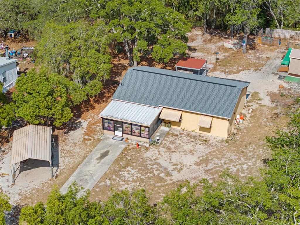 An aerial view shows a tan house with a gray roof, a screened porch, and carport — 17322 HARMONY DRIVE, HUDSON, FL